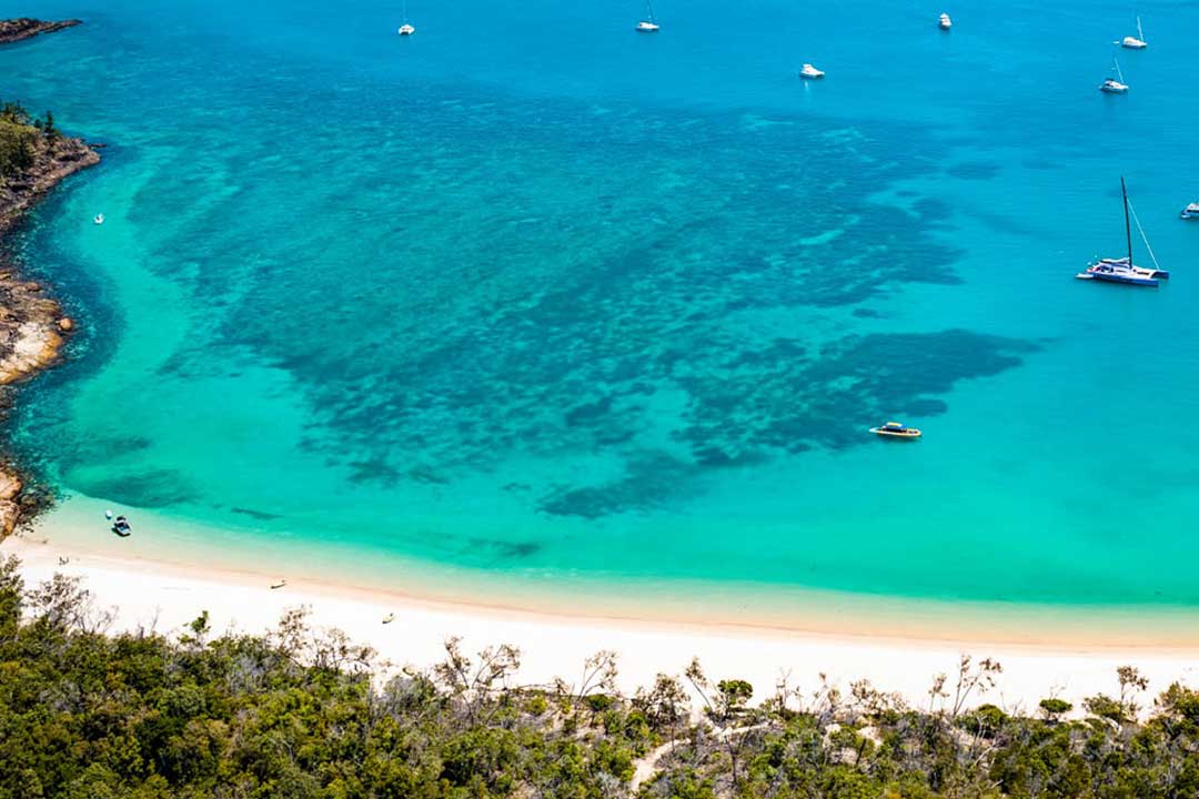 View of the beach at Chance Bay Whitsundays with boats anchored offshore and coral reefs